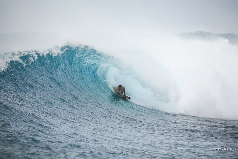 Bodyboarder riding inside a powerful barrel wave over a reef in the Maldives