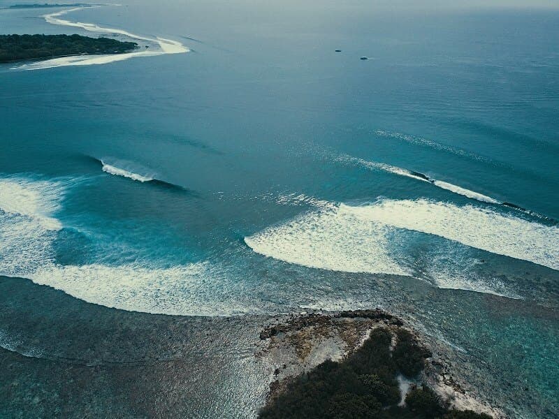 Aerial drone view of multiple reef breaks in the Maldives with waves breaking across a wide coral reef formation
