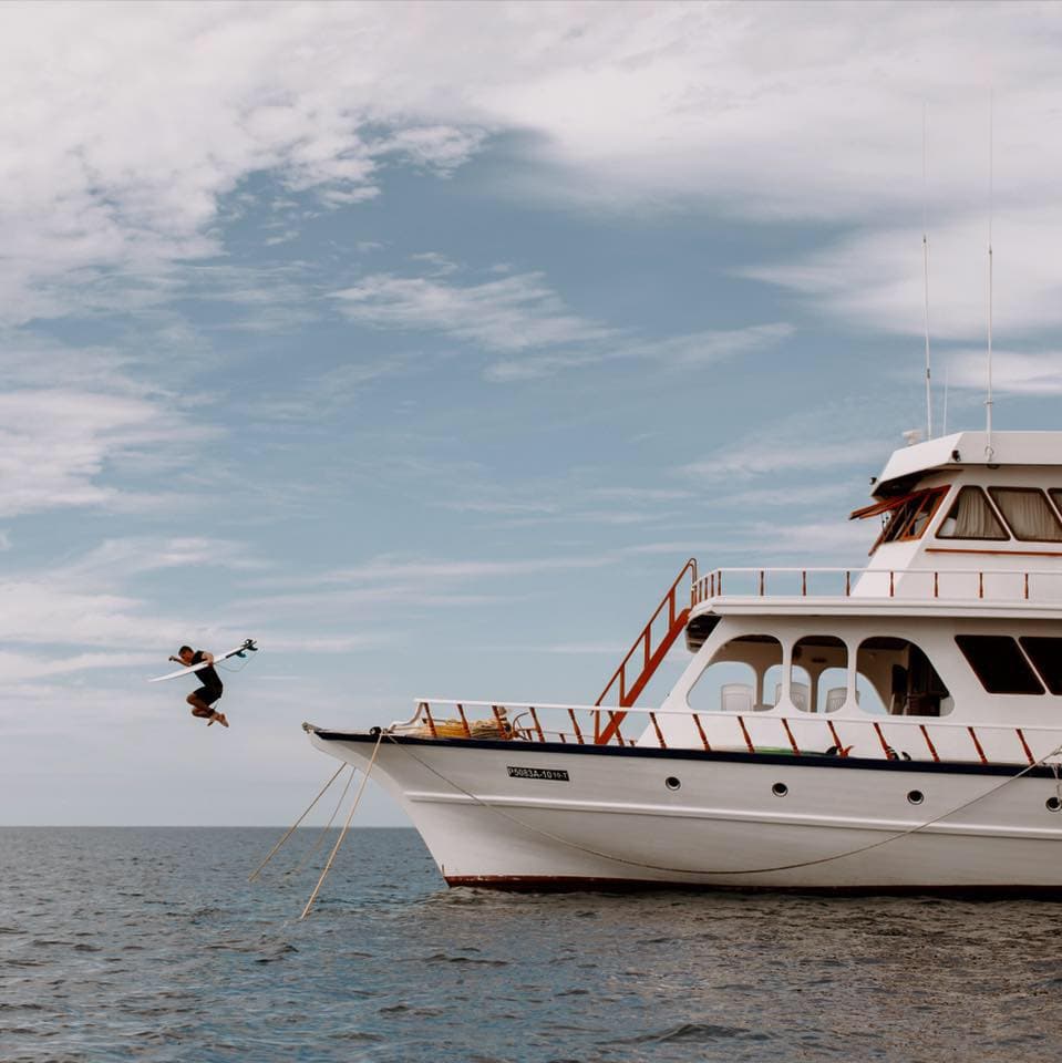 Surfer jumping from a liveaboard surf charter boat in the Maldives with surfboard and open ocean