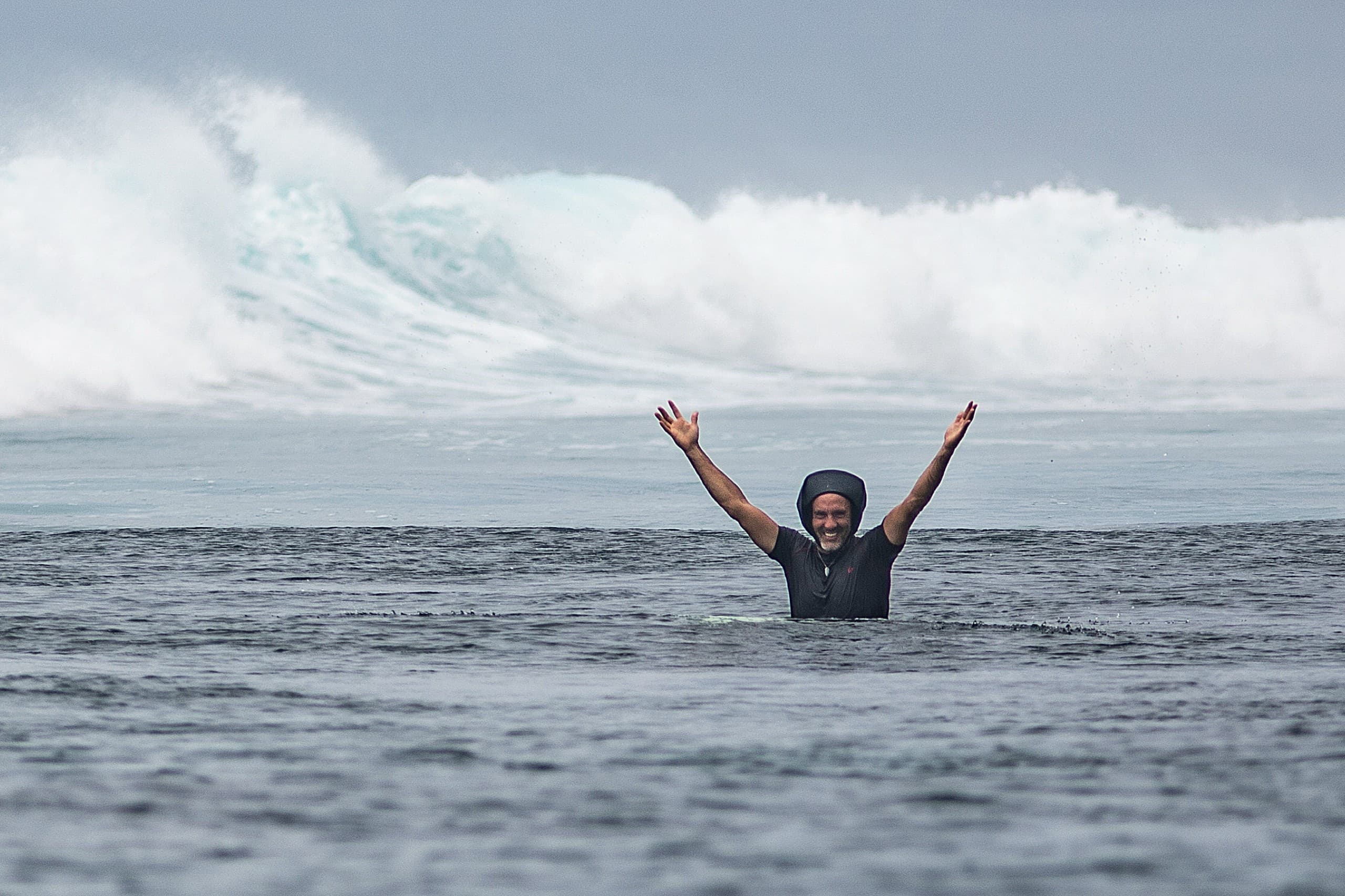 Surfer celebrating in the ocean with arms raised and a breaking wave behind in the Maldives
