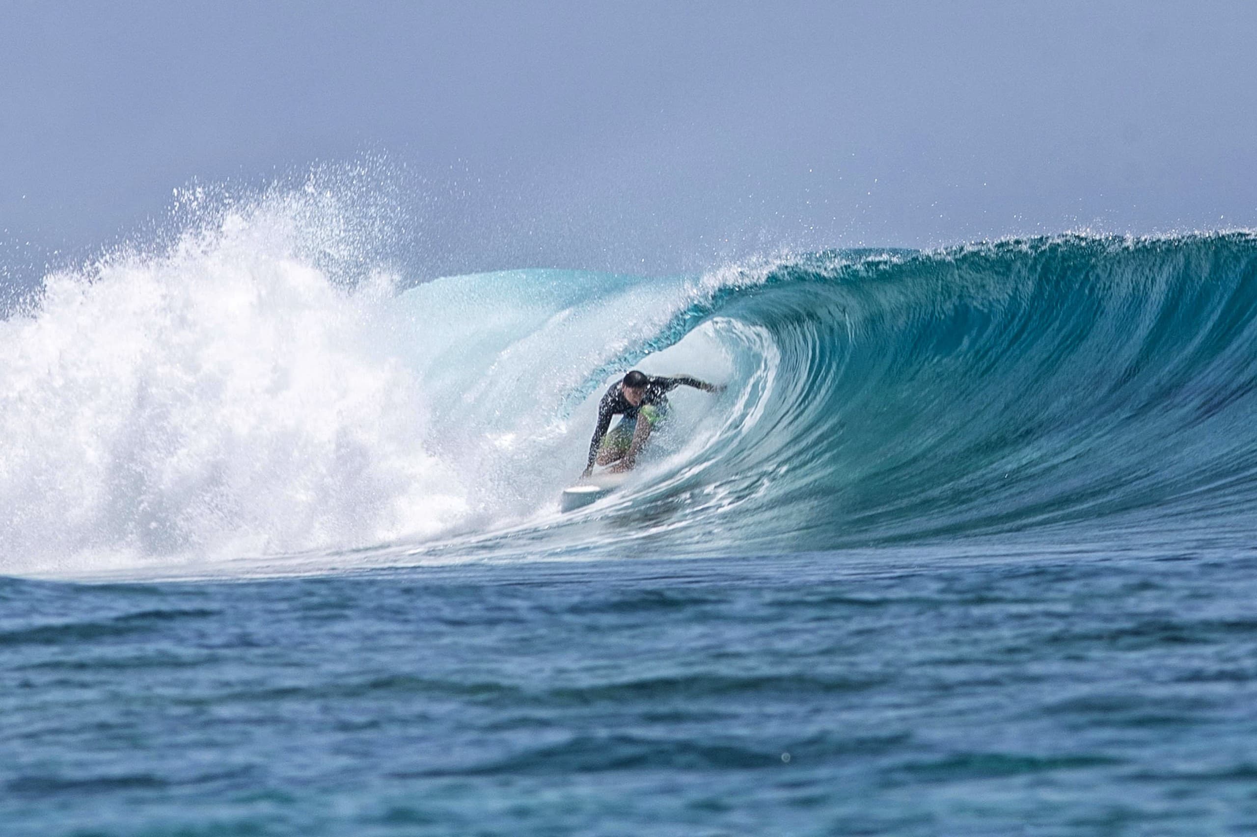 Surfer riding inside a hollow tube wave over a reef in the Maldives