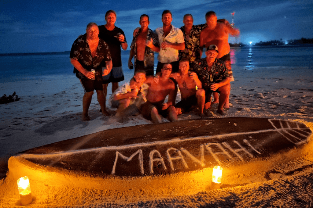 Group celebrating on Maldives beach at night with Maavahi written in sand and candle lights