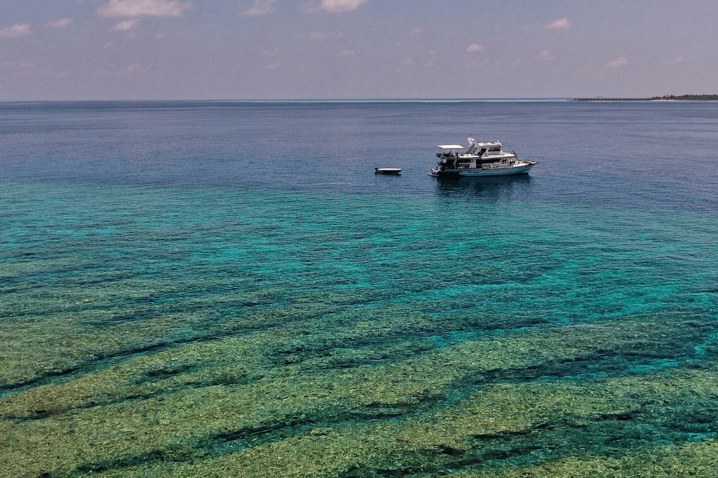 Aerial view of Maavahi liveaboard over coral reef in Maldives crystal clear lagoon