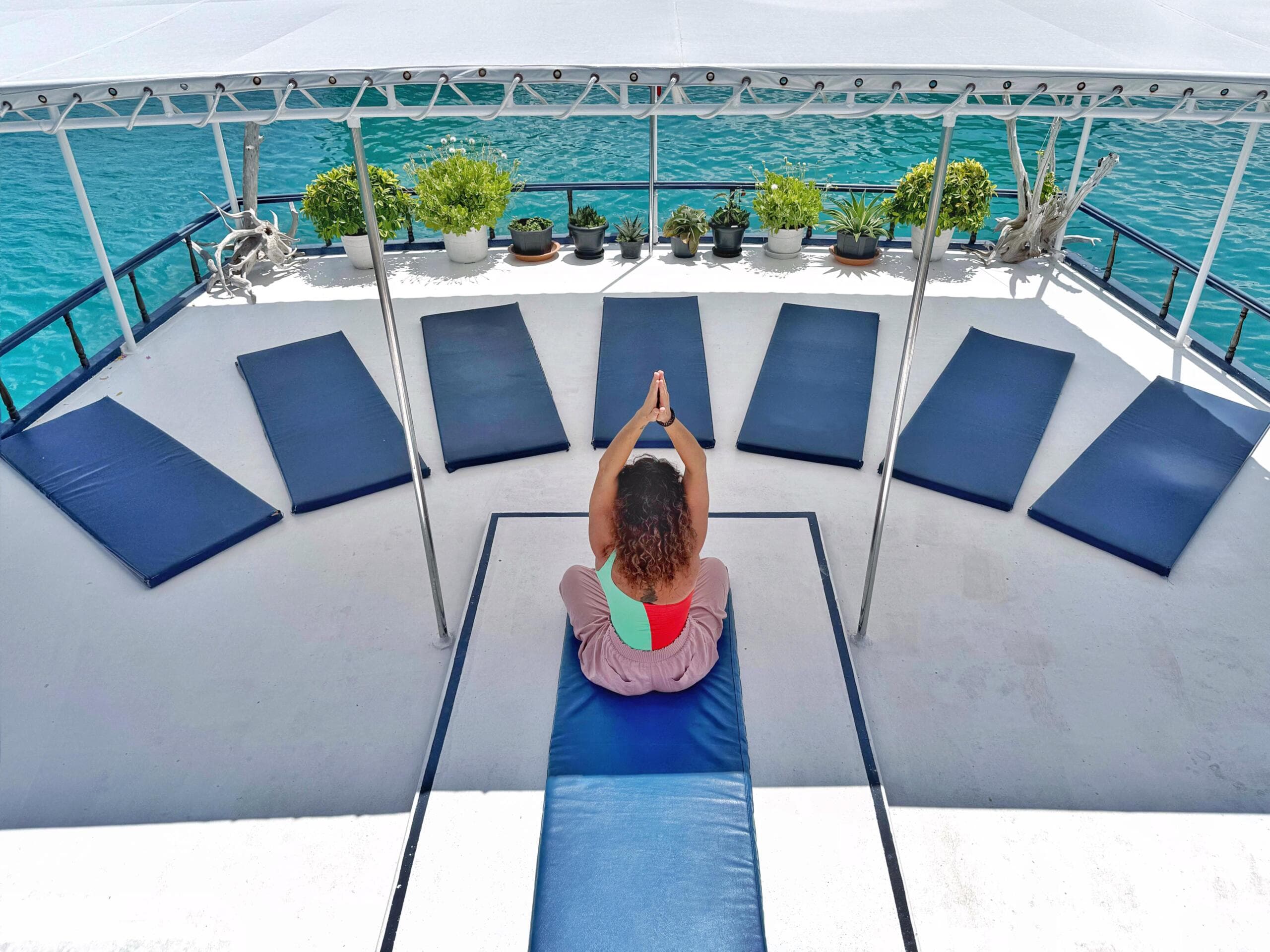Woman practicing yoga on Maavahi boat deck surrounded by ocean in Maldives retreat experience