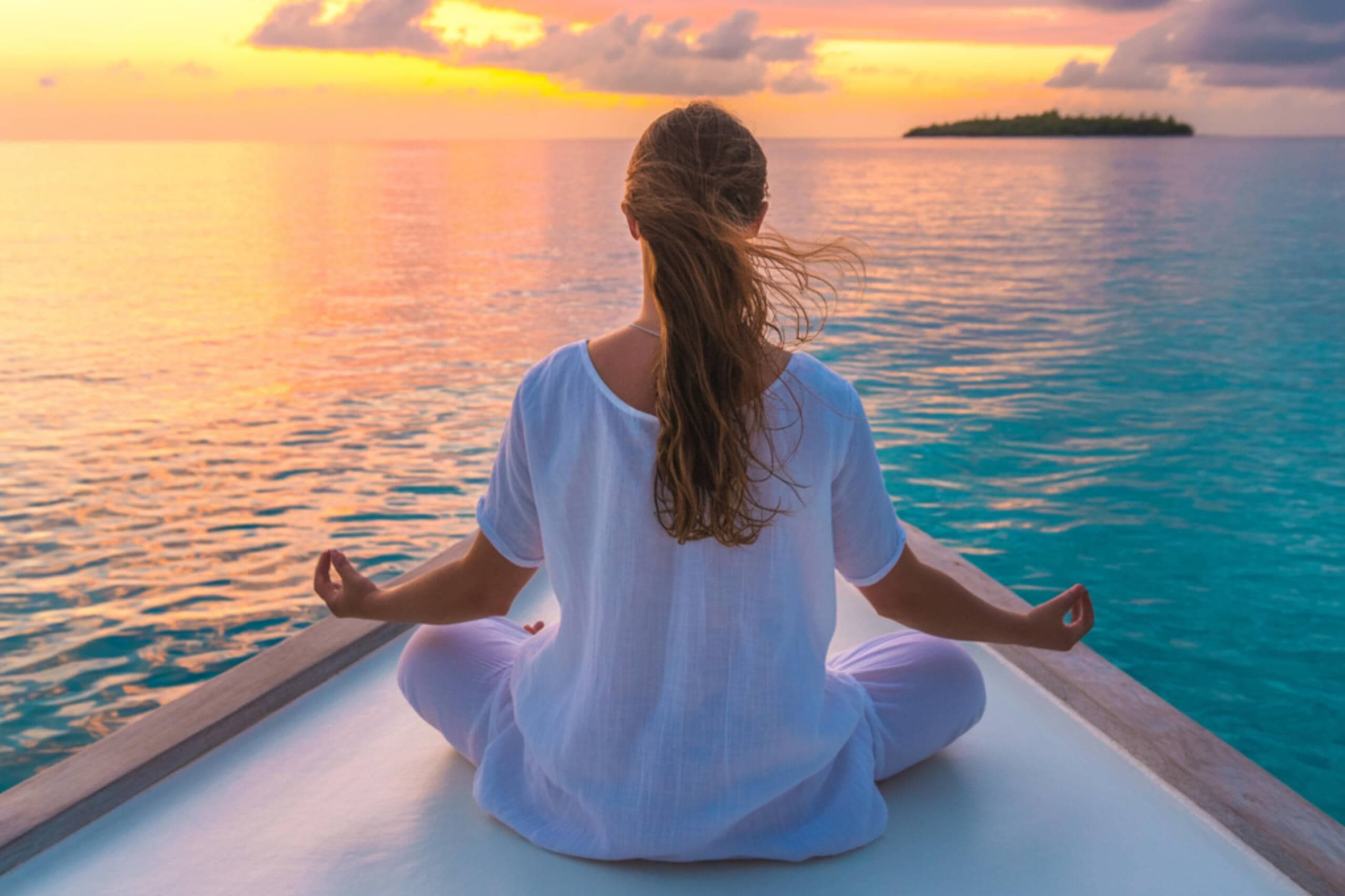 Woman meditating at sunset on the ocean during a Maldives yoga and wellness retreat